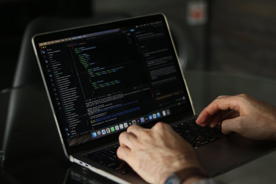 The image features a black laptop with a red backlit keyboard placed on a surface, displaying blurred lines of code on the screen with a neon blue and pink glow. Next to the laptop, there is a white b